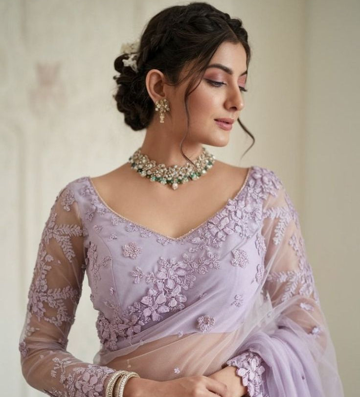 Woman wearing a lavender saree with intricate designs and jewelry against a neutral background